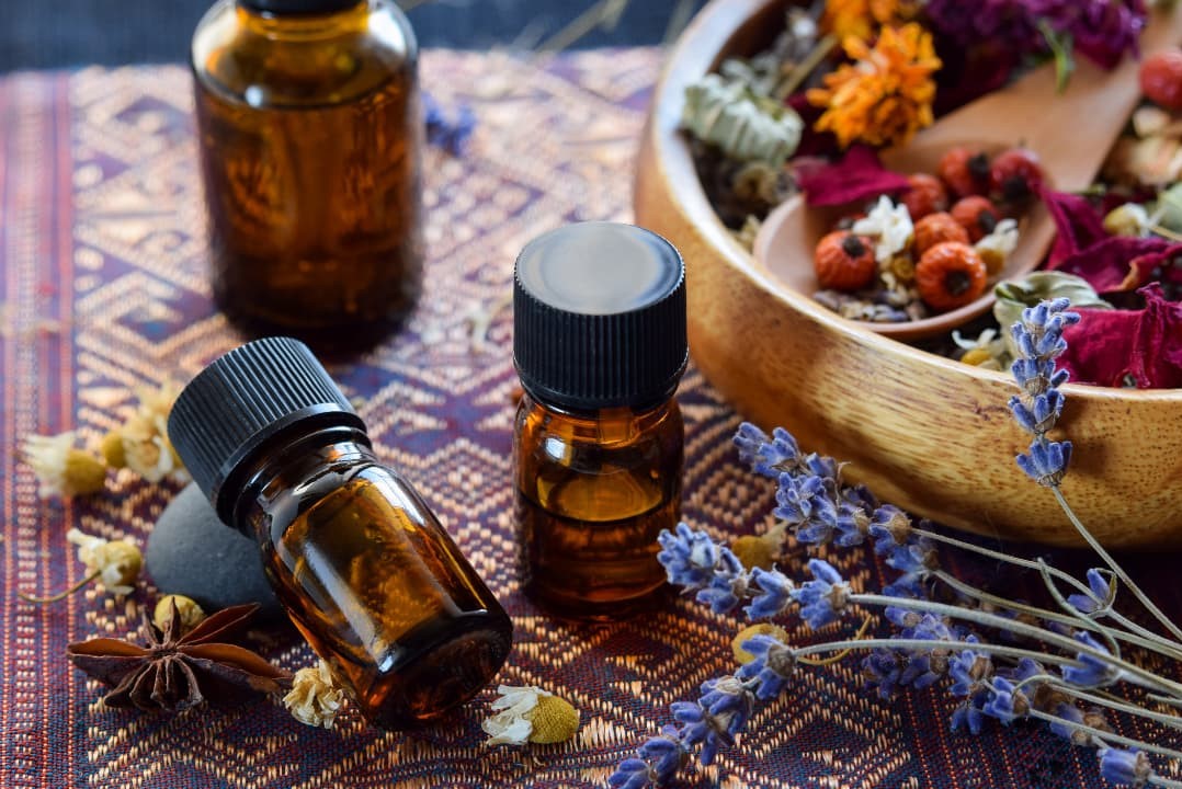 Essential oil bottles beside a wooden bowl of dried flowers