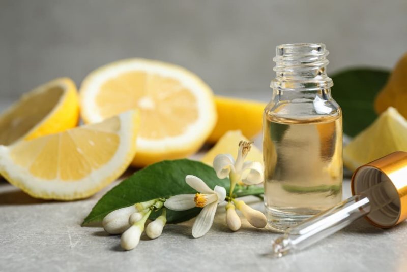 Lemon essential oil beside lemon slices and lemon flowers