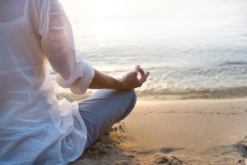 A woman meditating to become spiritually grounded on beach in lotus position