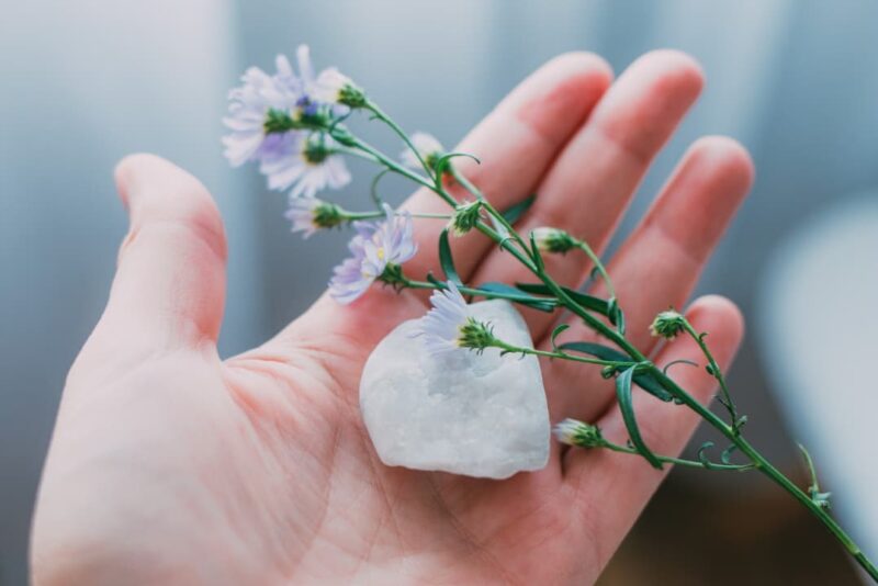 A person holding clear quartz and purple flowers